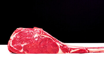 Fresh uncooked tomahawk steak on the bone on white cooking paper and black background. Prime cut of...