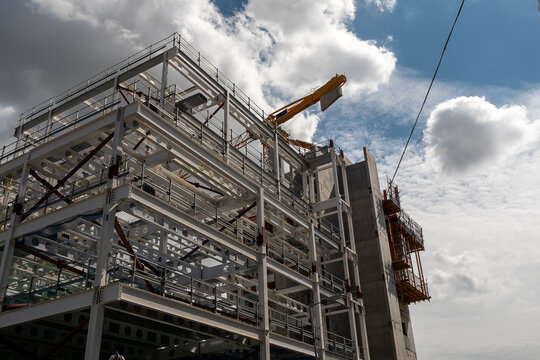 Construction of a modern tall building with metal frame. Developing residential and commercial high value property. Tall crane and cloudy sky in the background.