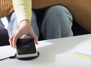Fototapeta premium Charging mobile phone battery with wireless charging device in the table. Smartphone charging on a charging pad.