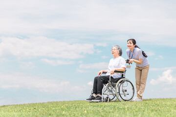 公園を散歩する介護士と車椅子の高齢者女性（青空）
