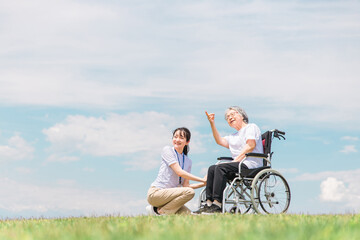 公園を散歩する介護士と車椅子の高齢者女性（外出介護）
