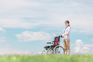 青空の中で車椅子を持つ介護士・作業療法士
