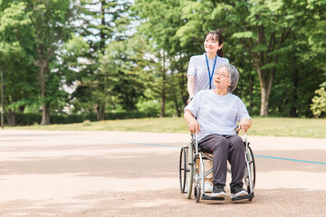 公園を散歩する介護士と車椅子の高齢者女性（緑）
