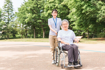 公園を散歩する介護士と車椅子の高齢者女性（緑）
