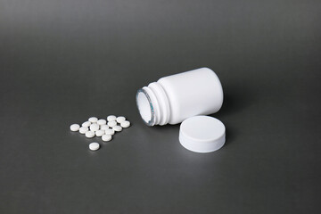 Unlabelled white plastic pill bottle. Poured out several small white pills. out side in black background