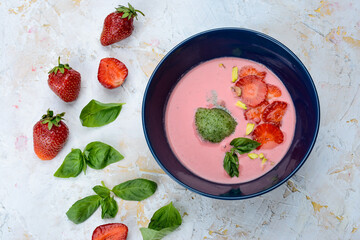 strawberry cream soup with strawberries in a blue plate on a light background with greens top view
