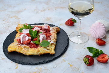 puff pastry with cheese and strawberries in a white plate on a white background with a glass of wine
