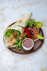 shawarma with chicken in pita bread on a plate with vegetables and pepper vertical photo
