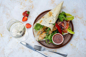 shawarma with chicken in pita bread on a plate with vegetables and pepper on a white background with a glass of wine
