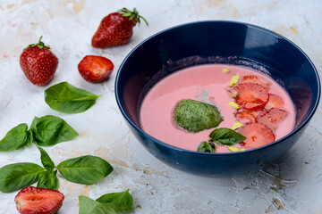 strawberry cream soup with strawberries in a blue plate on a light background with greens
