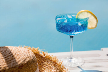 A glass of delicious blue cocktail "Blue Lagoon" and yellow lemons on the background of the pool. Alcoholic cocktail juicy fruit blue with curacao liqueur, ice cubes and a slice of lemon. 