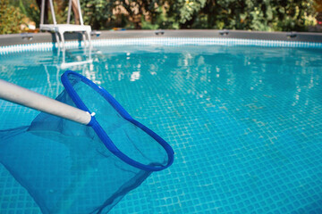 Cleaning a swimming pool with a metal frame with a net from leaves and dirt. Pool cleaner during work. Solar banner. The concept of summer holidays.