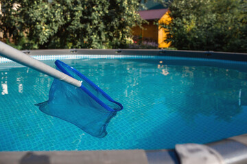Fototapeta na wymiar Cleaning a swimming pool with a metal frame with a net from leaves and dirt. Pool cleaner during work. Solar banner. The concept of summer holidays.