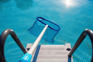 Cleaning a swimming pool with a metal frame with a net from leaves and dirt. Pool cleaner during...