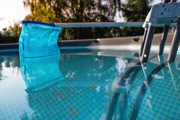 Cleaning of a swimming pool with a metal frame with a mesh from dirt. Pool cleaner during operation. Solar banner.The concept of summer holidays.Abstract blur and defocused background. 