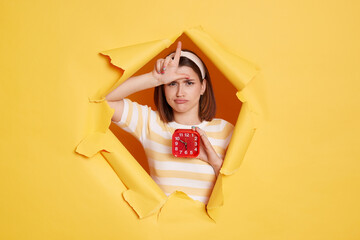 Horizontal shot of sad Caucasian woman wearing hair band and striped t shirt standing in yellow...