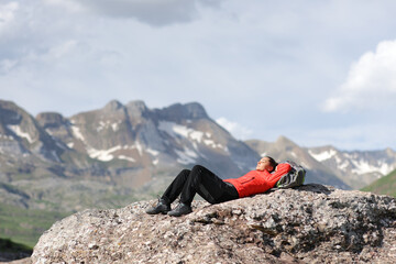 Tired hiker in red resting lying on the top of a high mountain