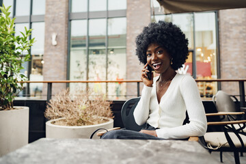 Smiling young african woman talking on cellphone at cafe