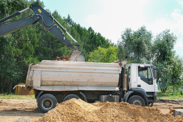 Obraz premium excavator with bucket loading sand into a truck at dirty construction site