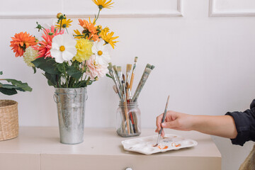 Close up of woman stirring the paint on the palette laying on dresser. Home decor. Hobby concept.