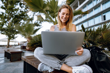 Young beautiful casual woman working on a laptop sitting on the bench in the street