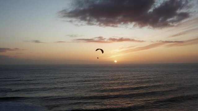 Silhouette of paraglider parachute flying over ocean. Beautiful golden light at sunset.