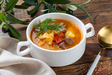 Meat and vegetables soup with parsley in bowl over rustic wooden background close up