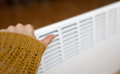 Woman warming her hand on a warm electric heater in a cold winter day at home. Saving electricity,...