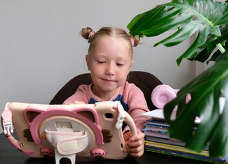 A little girl uses a tablet for distance learning. Home schooling, online education. Child use...