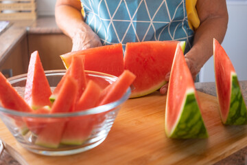 Female hands cutting a fresh watermelon in slices and then in triangles - healthy eating concept