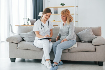 Nurse is giving prescription. Senior woman have consultation by young female doctor indoors