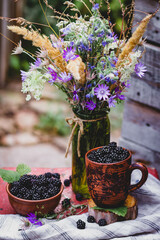 A bouquet of wildflowers and blackberries in a ceramic bowl . Still life with fresh berries in a rustic style