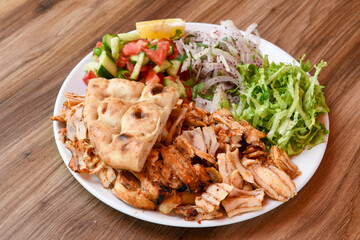 Turkish and Arabic Traditional Ramadan chicken doner kebab with tasty tomato sauce and rice or turkish pilav in white plate on wood table background. (Pilav ustu tavuk doner)