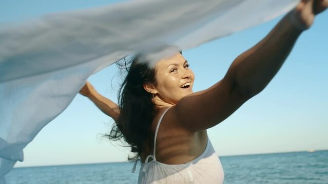 Beautiful young woman girl holding pareo fabric in the wind overlooking the sea