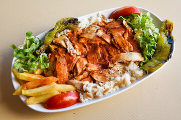 Turkish and Arabic Traditional Ramadan chicken doner kebab with tasty tomato sauce and rice or turkish pilav in white plate on wood table background. (Pilav ustu tavuk doner)