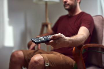 Adult man watching tv at home and holding a remote.