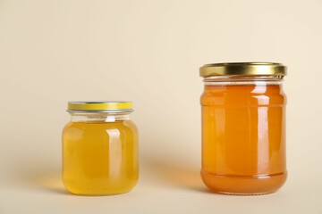Jars with different types of organic honey on beige background