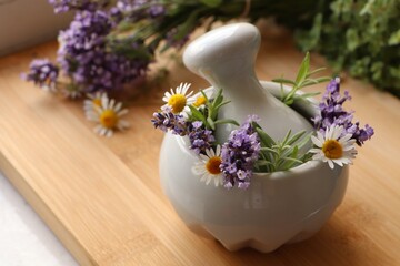 Mortar with fresh lavender, chamomile flowers, rosemary and pestle on wooden table, space for text