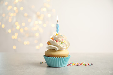 Birthday cupcake with candle on light grey table against blurred lights