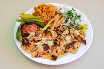 Turkish and Arabic Traditional Ramadan chicken doner kebab with tasty tomato sauce and rice or turkish pilav in white plate on wood table background. (Pilav ustu tavuk doner)