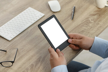 Man using e-book reader at wooden table, closeup