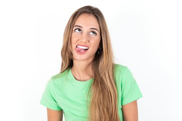 young beautiful woman wearing green T-shirt over white background showing grimace face crossing eyes and showing tongue. Being funny and crazy