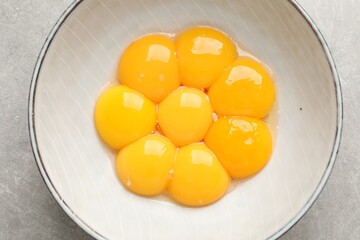 Bowl with raw egg yolks on grey table, top view