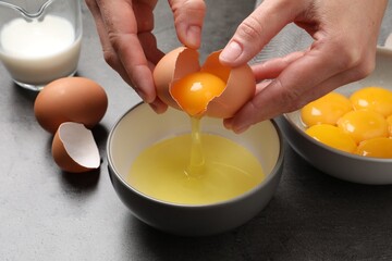 Woman separating egg yolk from white over bowl at grey table, closeup