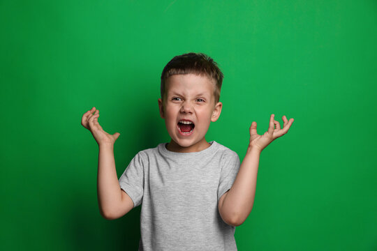Angry little boy screaming on green background. Aggressive behavior