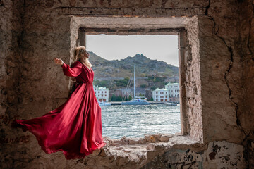 View of Balaklava Bay through an arched balcony in oriental style. The girl in a long red dress stands with her back. Abandoned mansion on the Black Sea coast