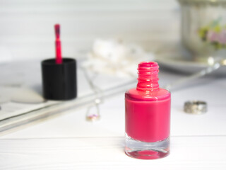 A glass jar of bright pink women's nail polish stands on a table, on a white background