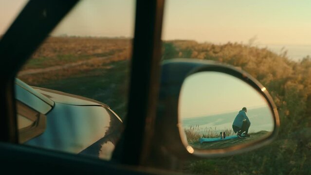 Tourist girl looking at the sunset in the reflection of the car mirror