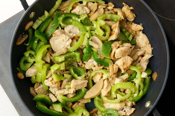 Chopped chicken fillet with mushroom and green peppers fried on frying pan. Cooking process close up.