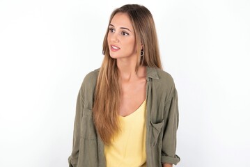 Fototapeta premium young beautiful woman wearing green overshirt over white background stares aside with wondered expression has speechless expression. Embarrassed model looks in surprise